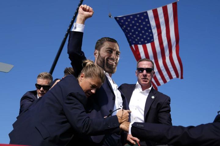 GigaChad raises fist in victory with security detail around him.